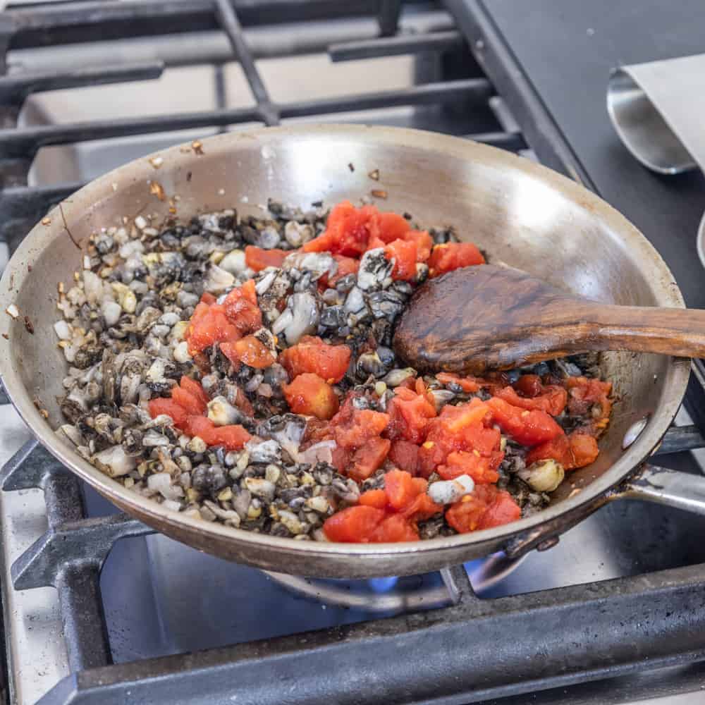 adding tomatoes to huitlacoche cooking in a pan