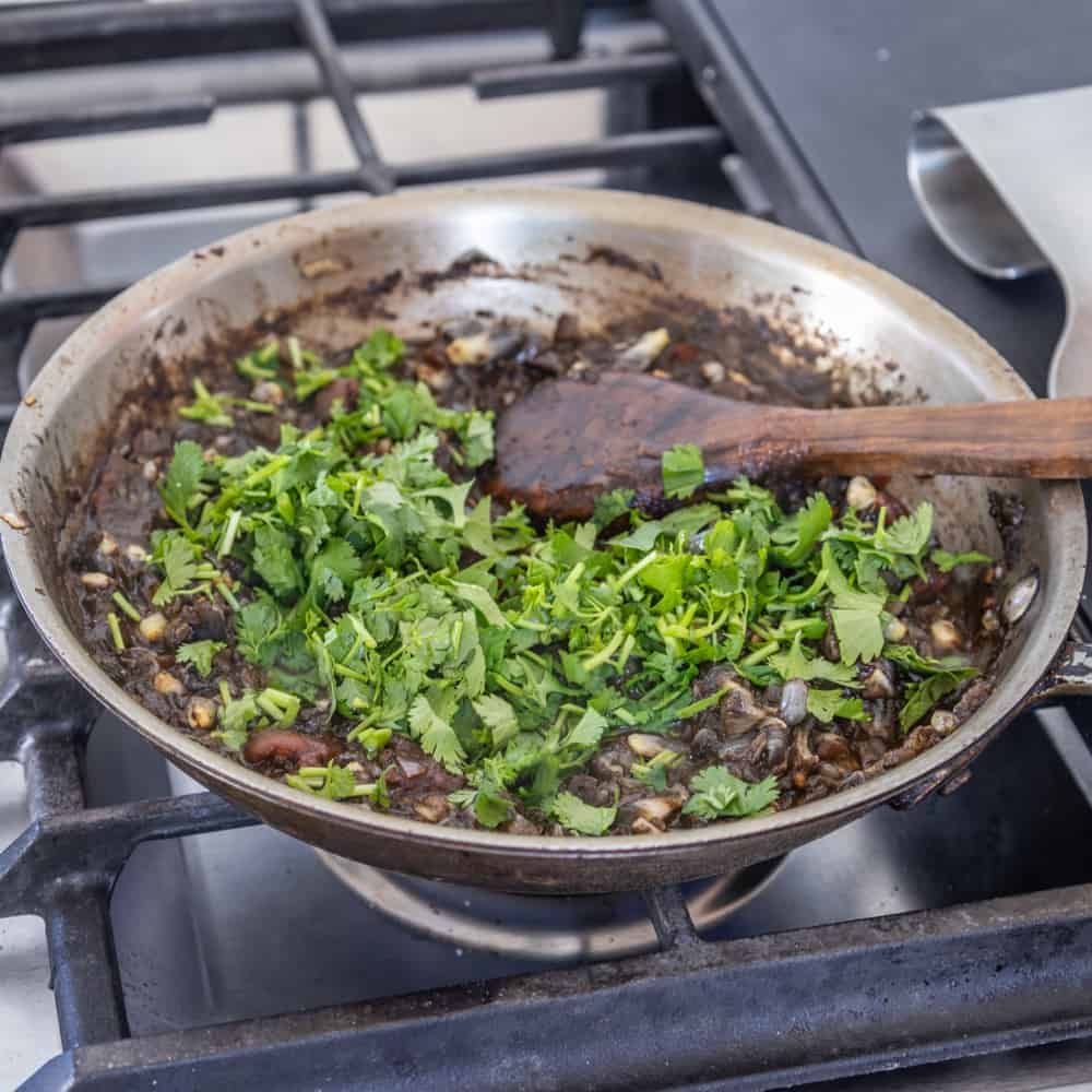 adding cilantro to a pan cooking huitlacoche