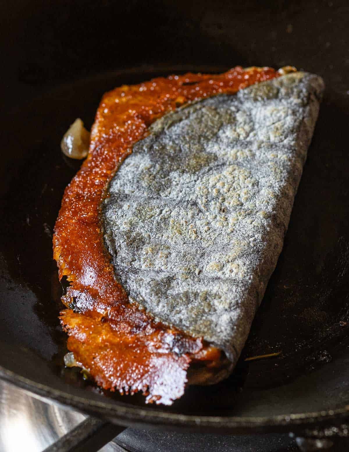 A huitlacoche quesadilla in a blue corn tortilla with a golden brown ring of crispy cheese around the edge.