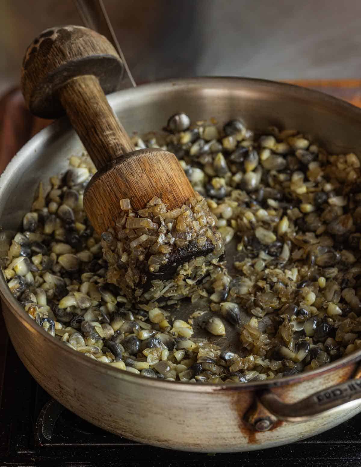 Mashing huitlacoche kernels with a wooden mallet to mimic a metate.