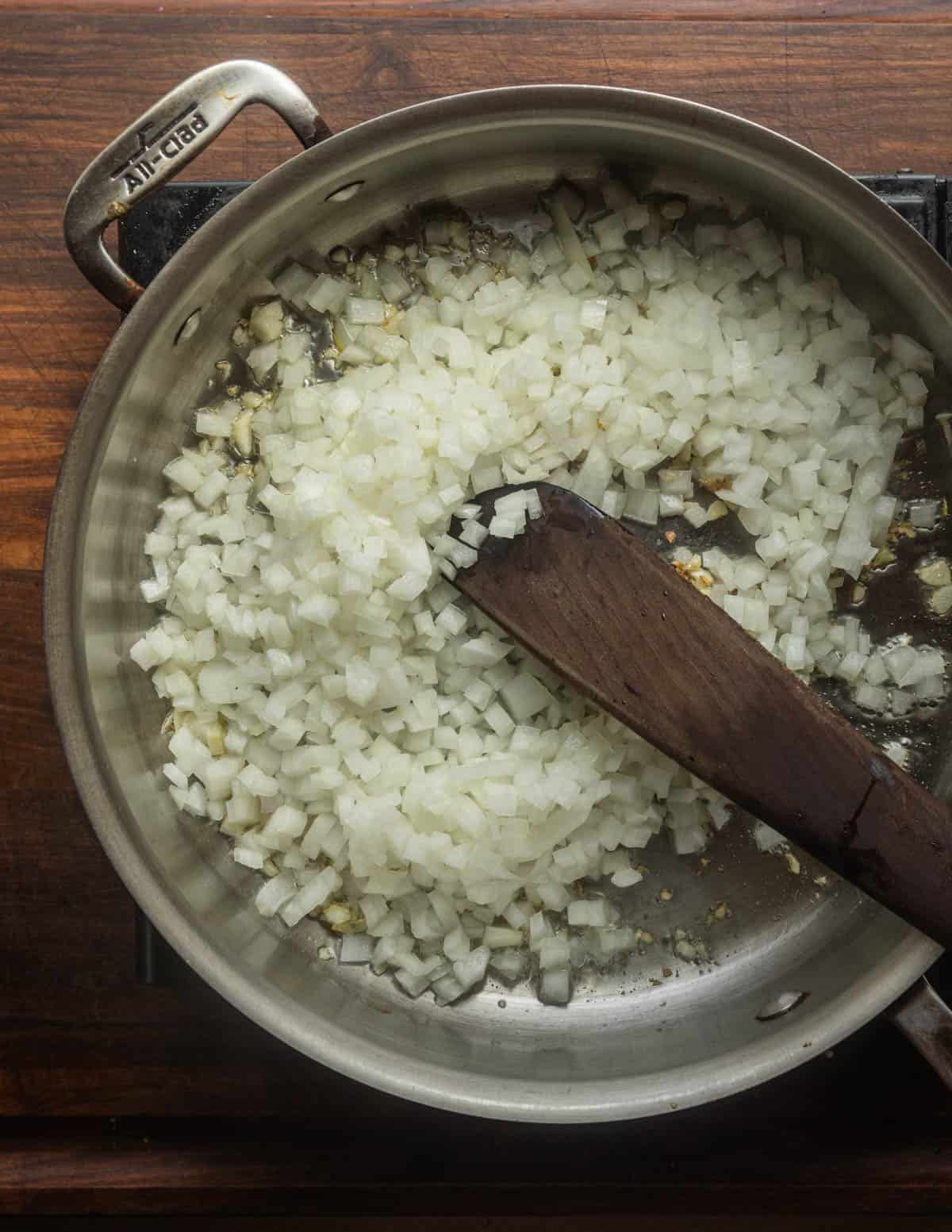 Adding finely chopped white onion to a pan with garlic.