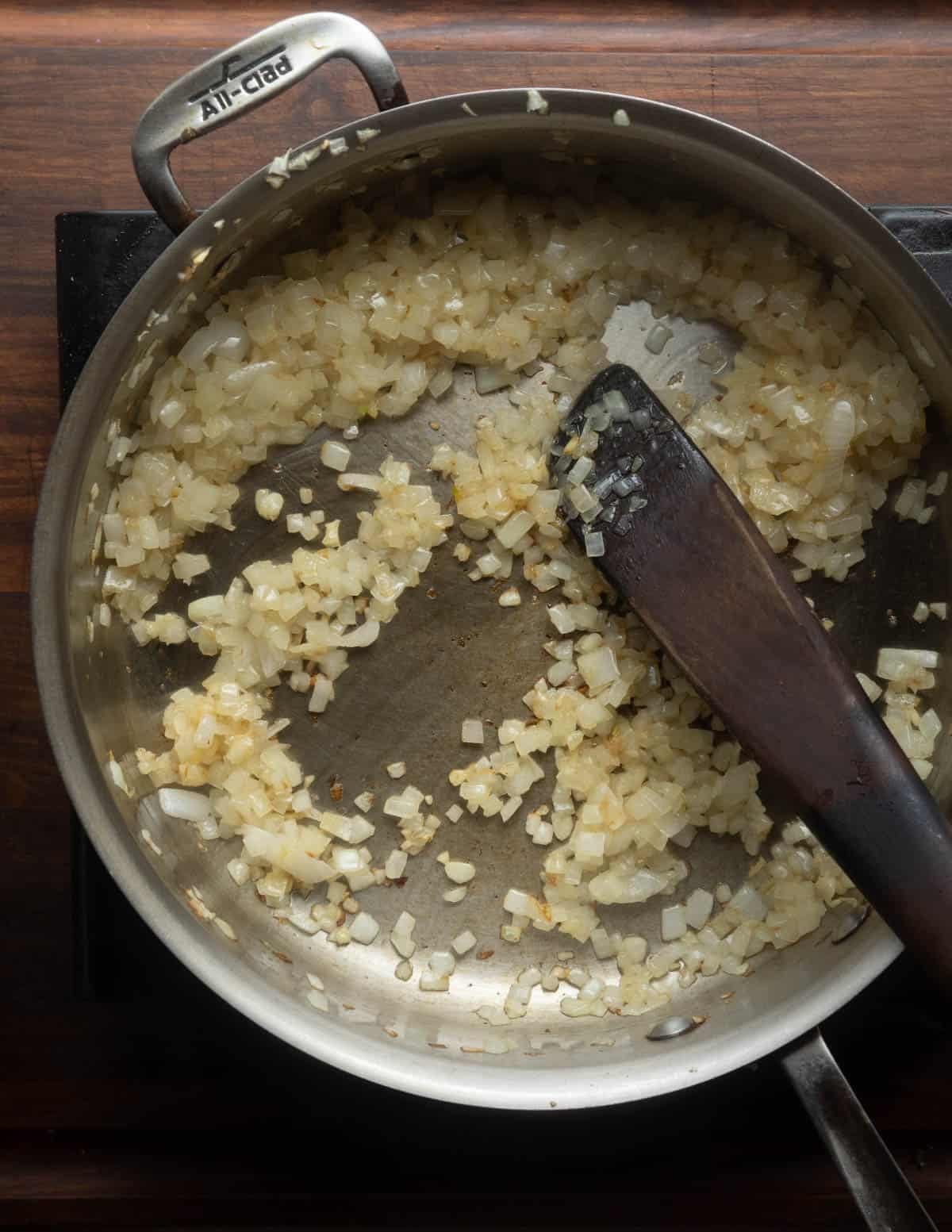 Stirring a pan with onion and garlic with a wooden spatula.