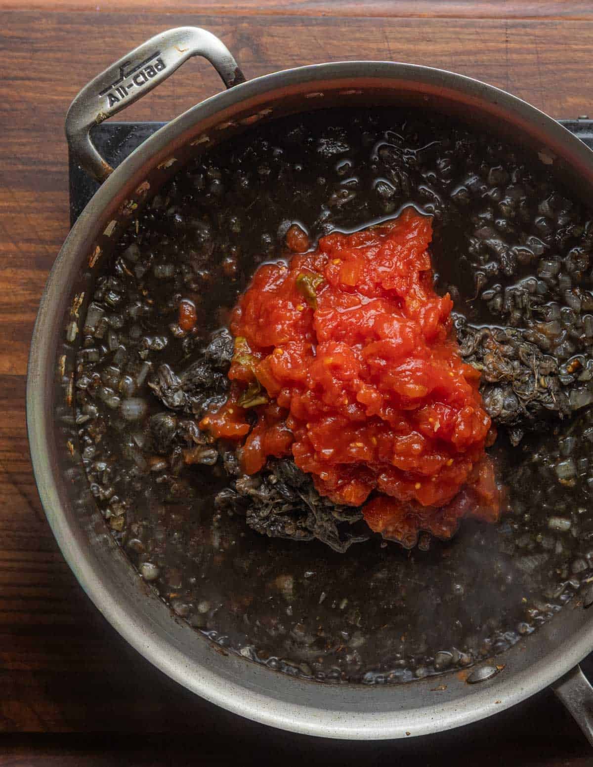 Adding chopped tomatoes and their juice to a pan of huitlacoche.
