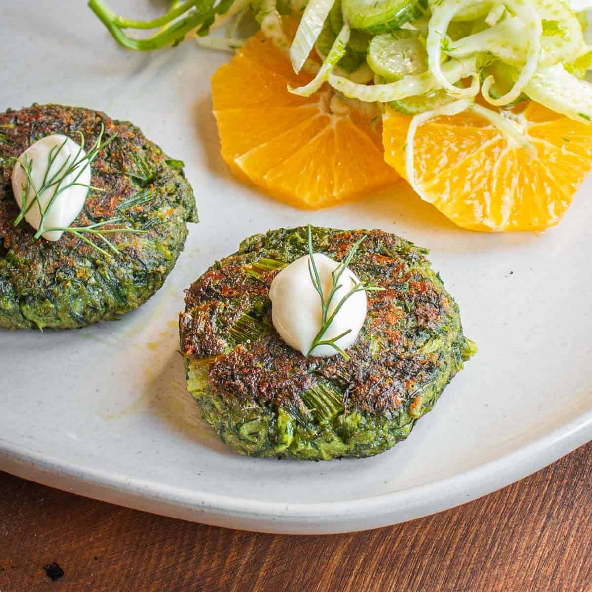 Wild fennel frond cakes on a plate with shaved fennel and orange slices.