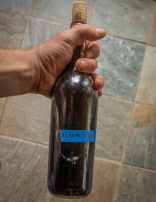 A hand holding a bottle of homemade walnut wine. 