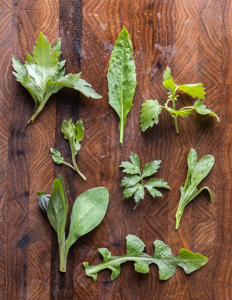 8 leaves of edible wild plants laid out on a butternut board