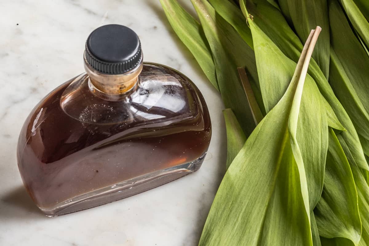 Fermented ramp leaf garum in an apothecary bottle next to ramp leaves