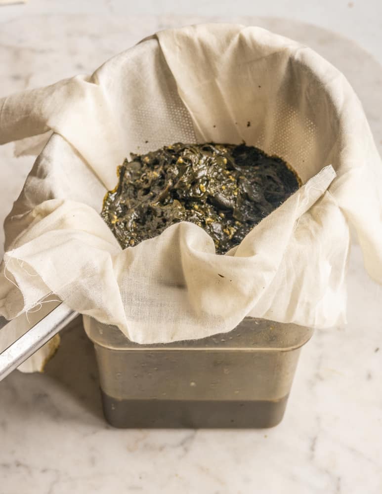 Straining fermented ramp leaf garum through muslin in a chinois strainer