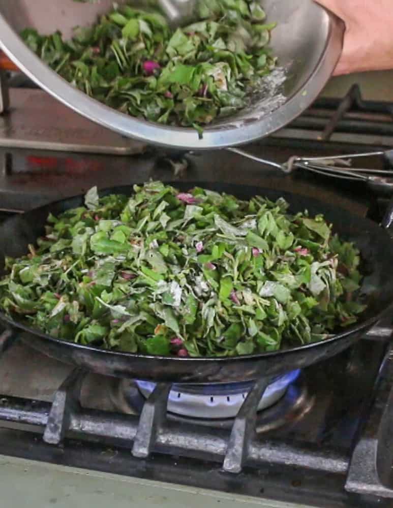 putting the seasoned greens into a hot carbon steel pan