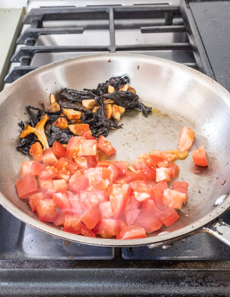 adding fresh tomatoes to mushrooms and garlic in a pan