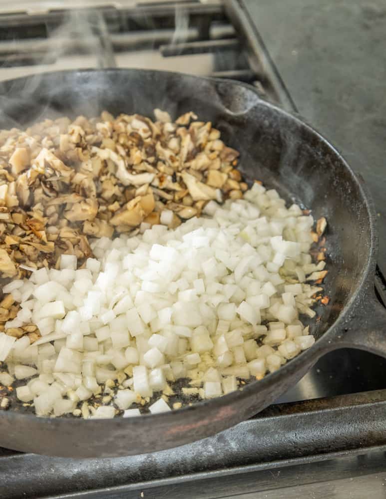 Adding onions to wild mushrooms for filling in a cast iron skillet