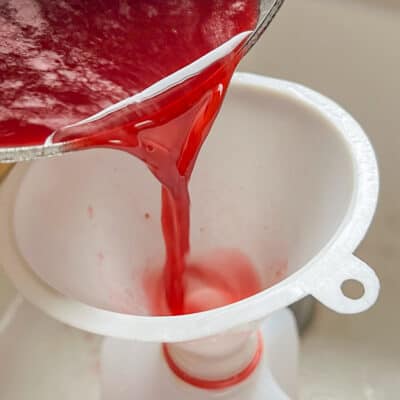 pouring berry cider through a funnel into a jug