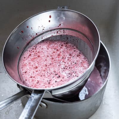 straining aronia berry cider through a chinois