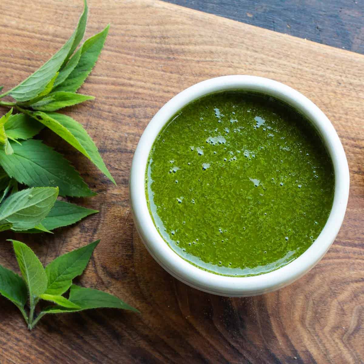 a bowl of green herb sauce next to fresh bee balm leaves 