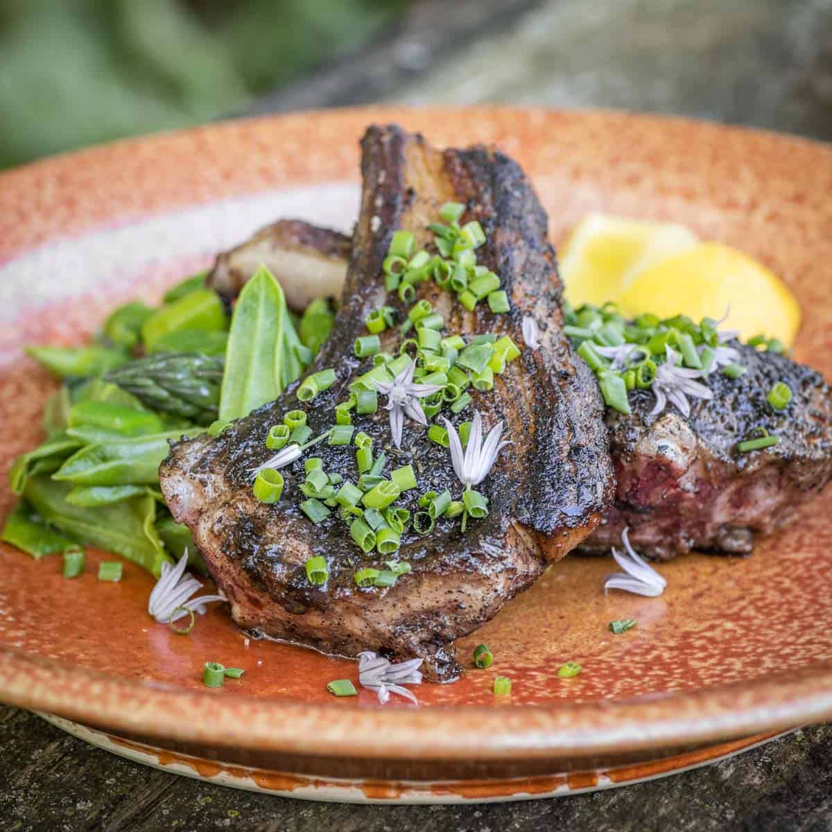 mushroom crusted lamb chop on a plate with chive flowers and greens 