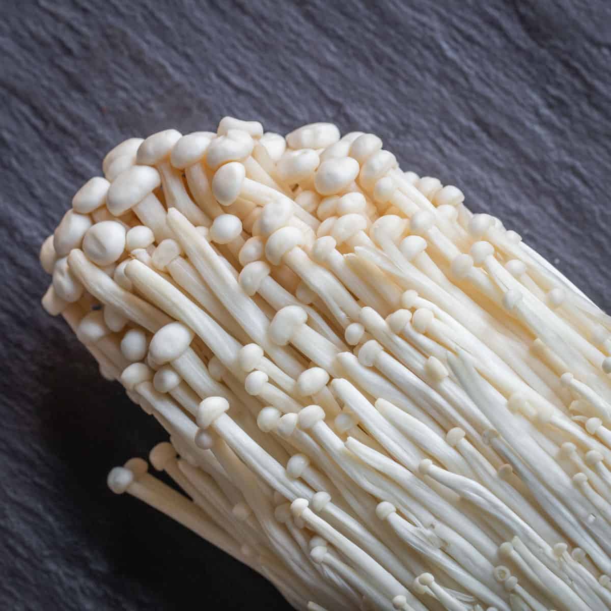 a cluster of white enoki mushrooms on a piece of slate. 