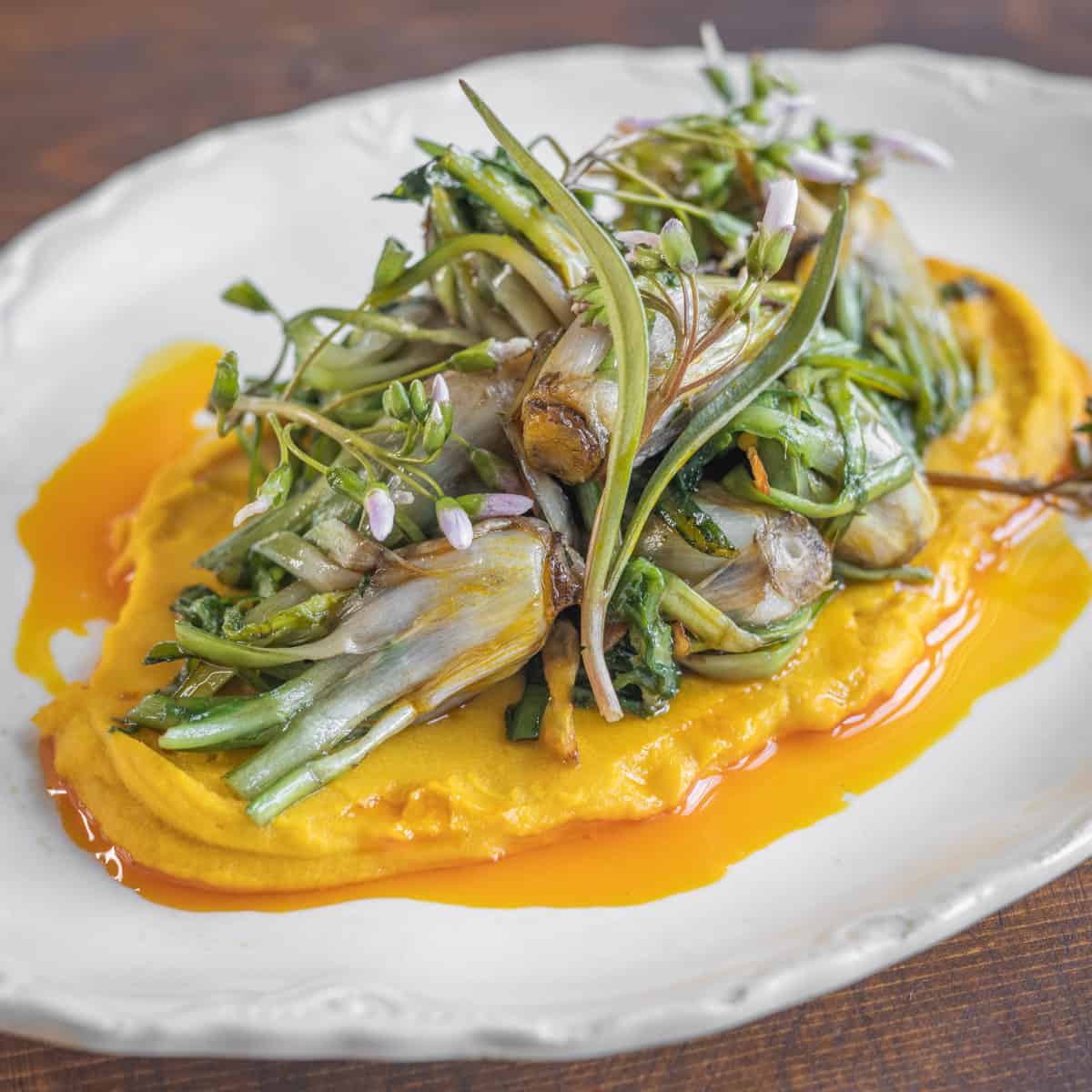 cooked dandelion crowns on a bed of orange hummus with spring beauty greens 