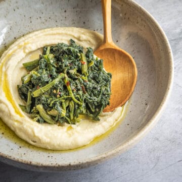 a bowl of fava bean puree with greens and wooden spoon