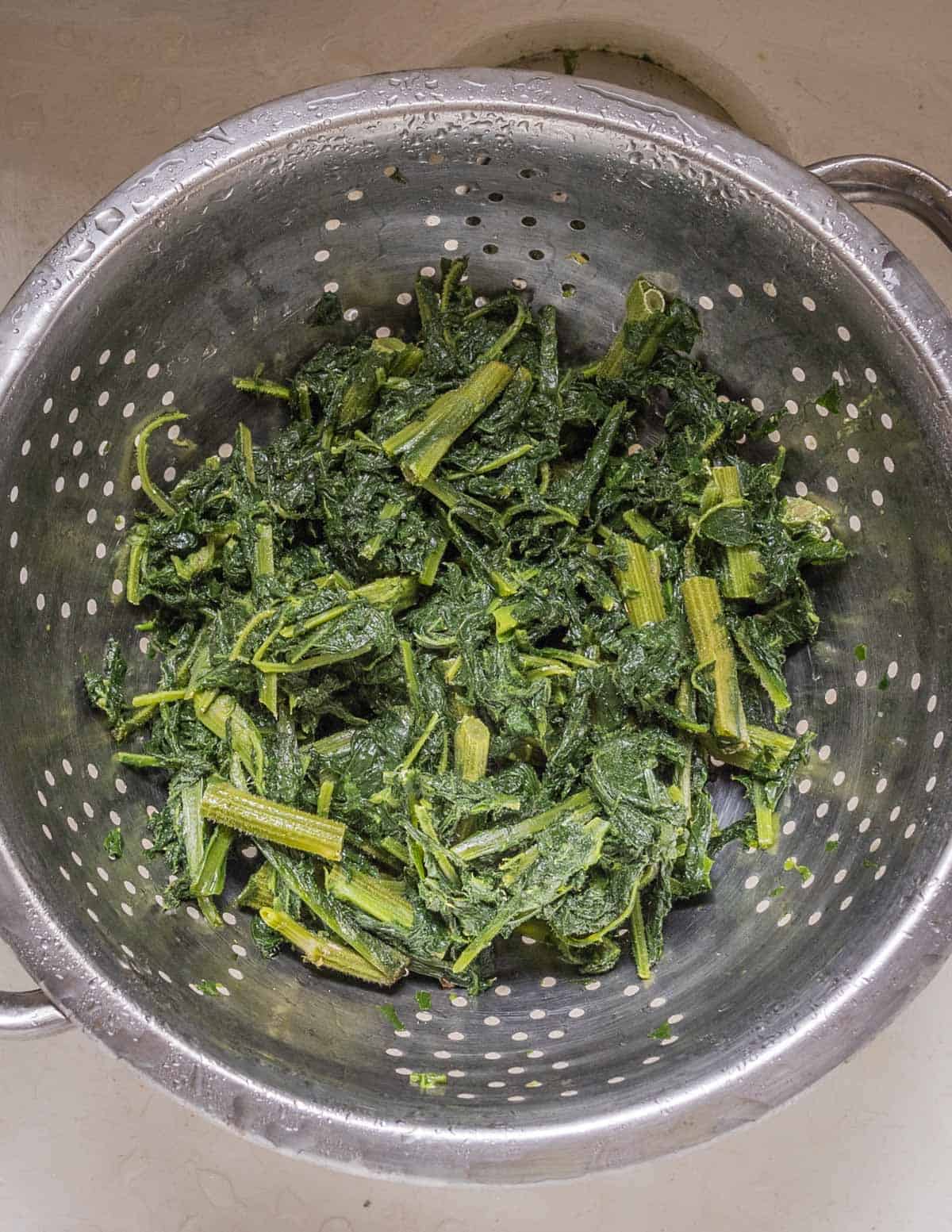 cooked foraged greens draining in a colander.