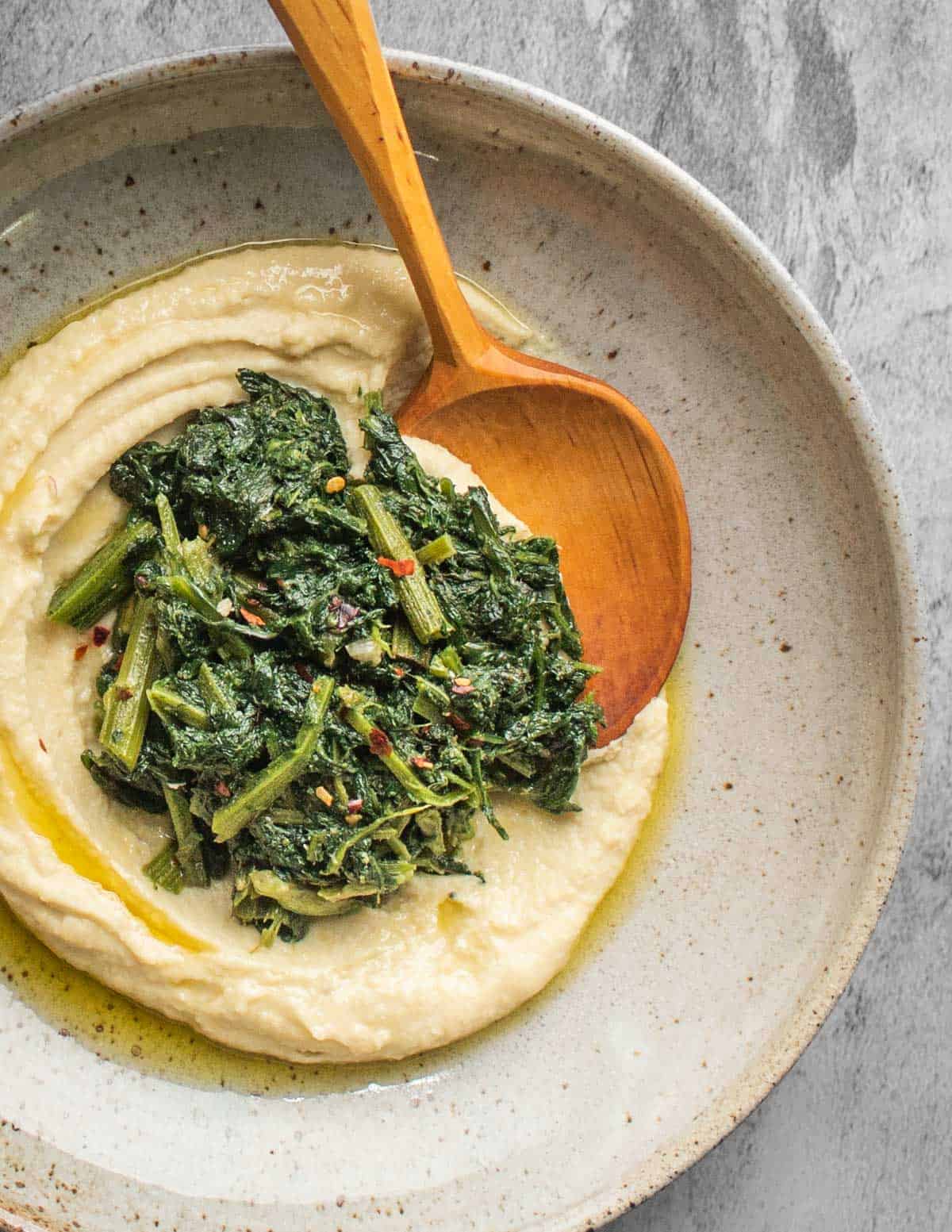 fave bean puree in a bowl with cooked greens, garlic, chili and olive oil. 