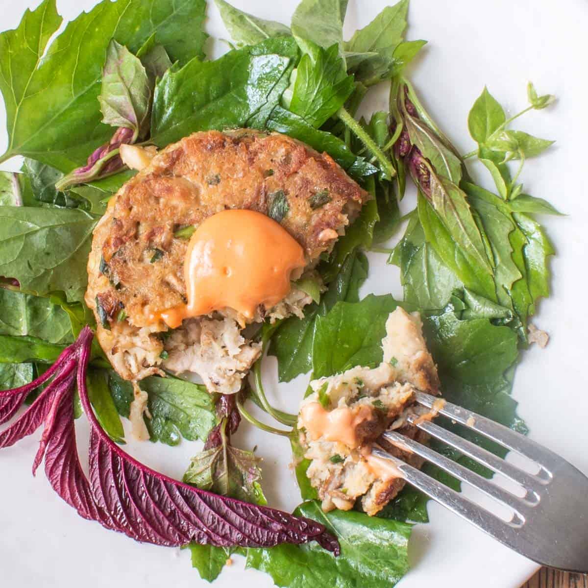 lions mane mushroom crabcake on a plate with sriracha aioli and greens