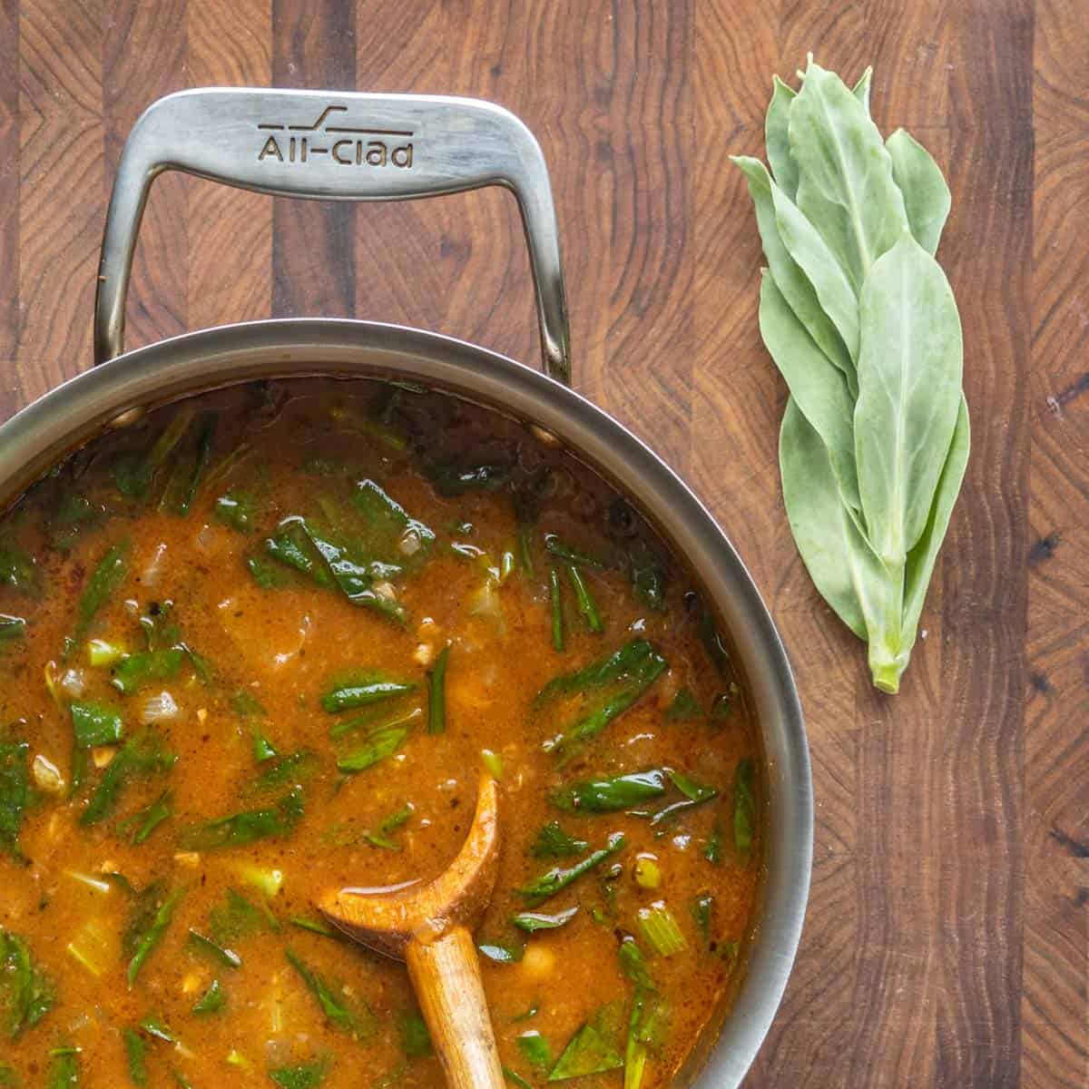 A soup in a pot with chickpeas and greens. 