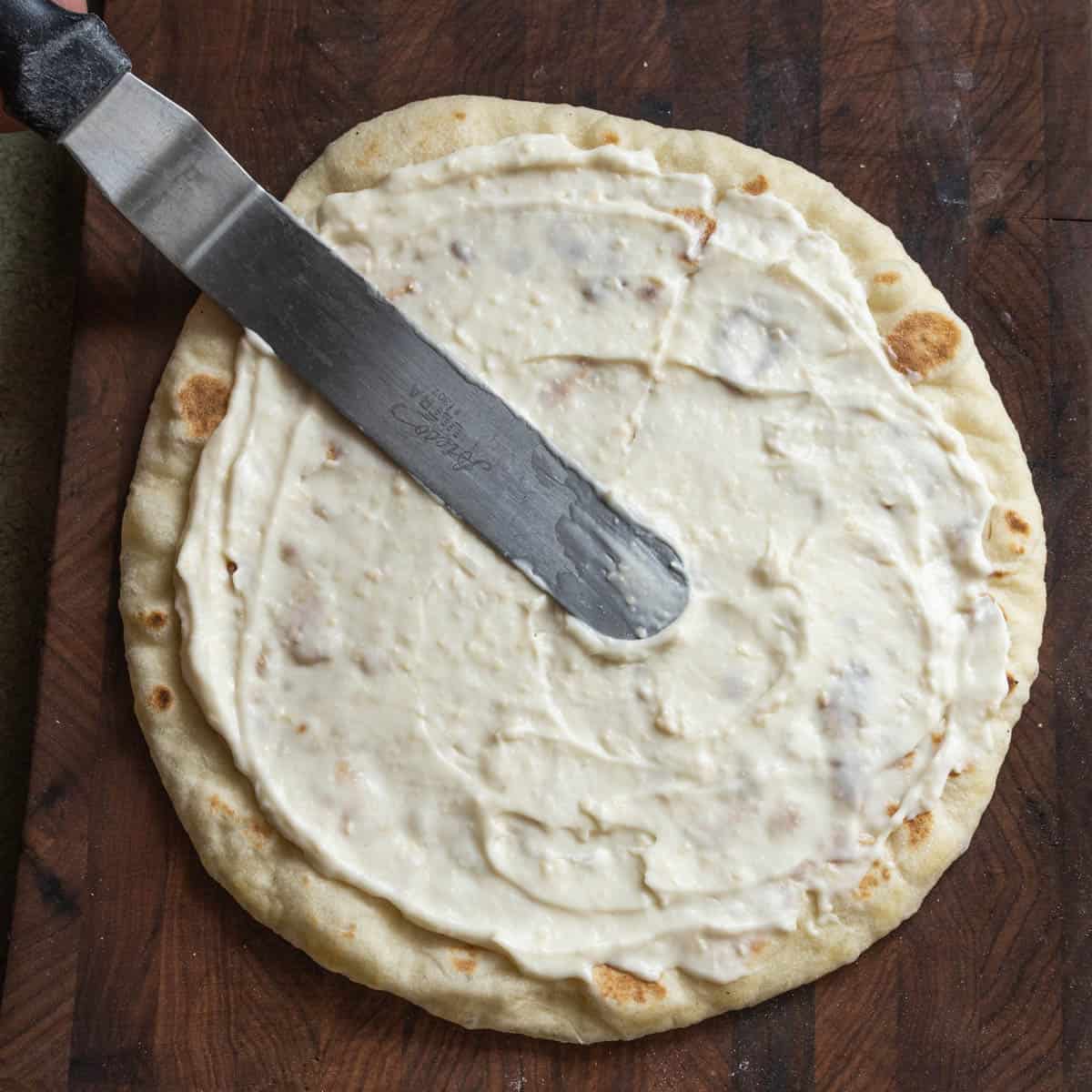 spreading a pizza crust with white sauce