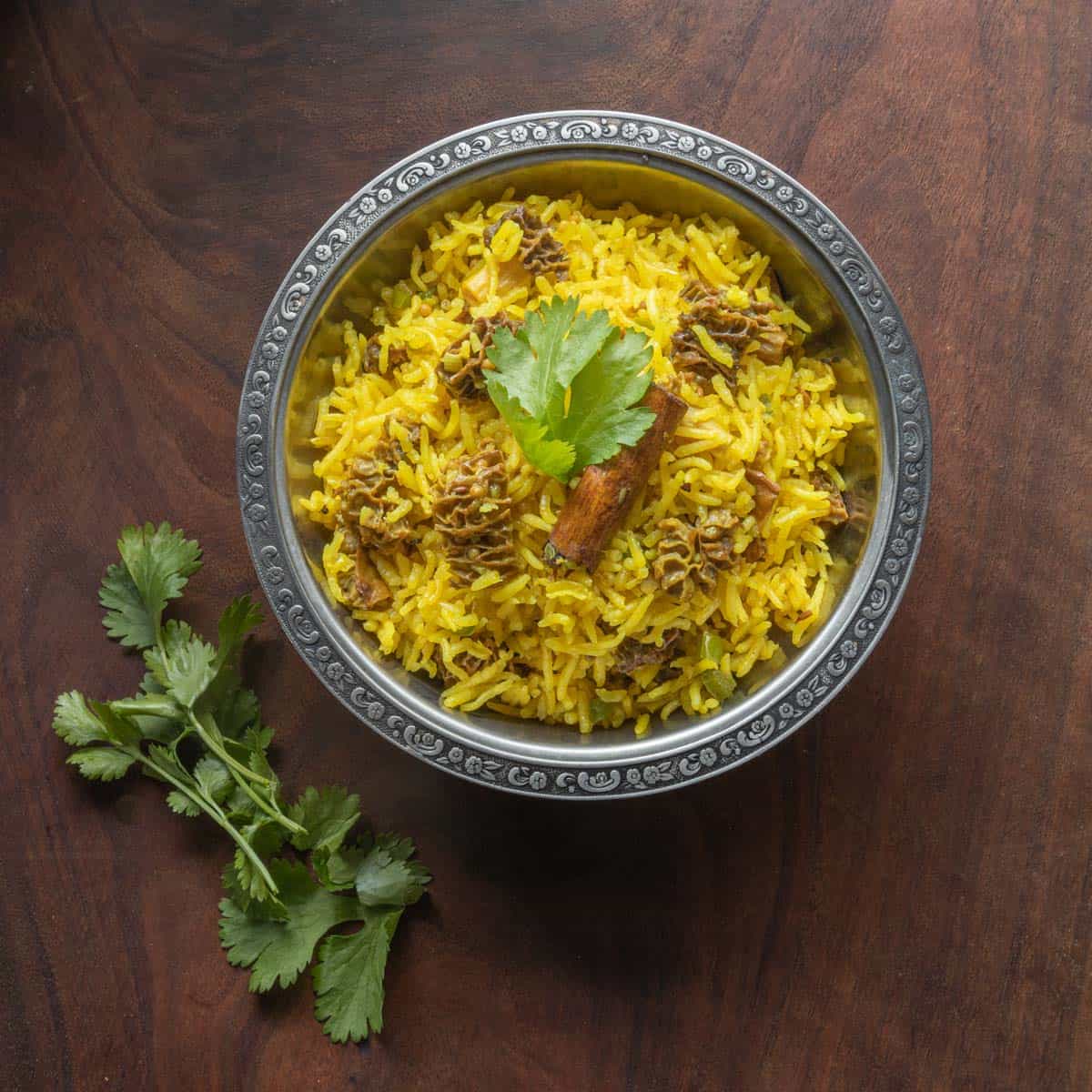 a bowl of yellow rice and mushrooms with coriander leaves