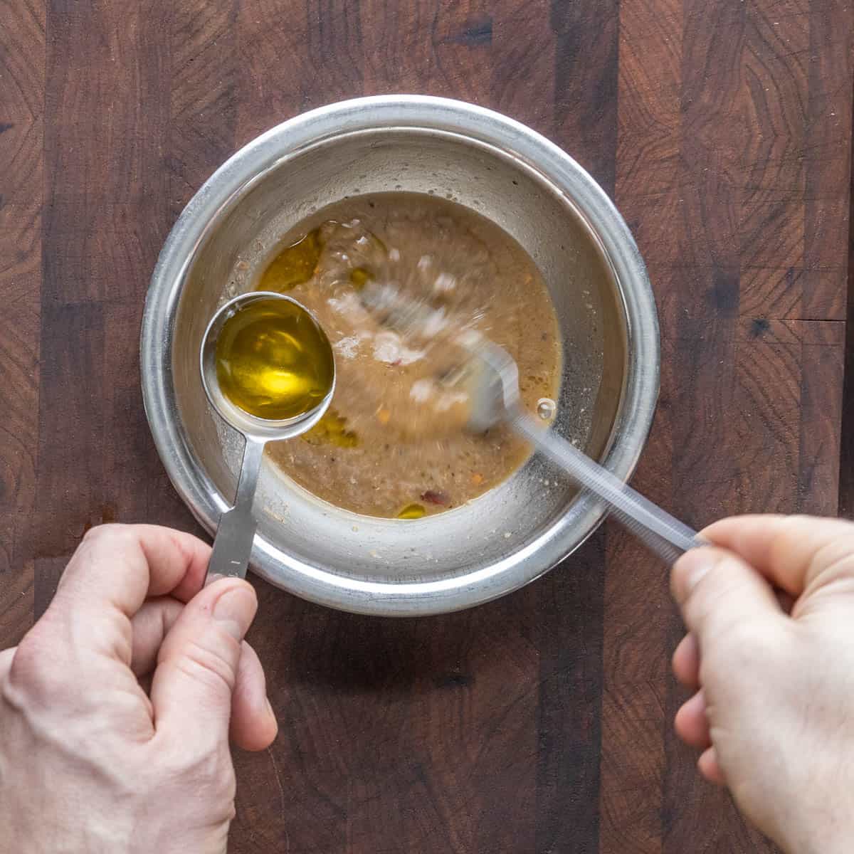 Whisking olive oil into a bowl of anchovy vinaigrette