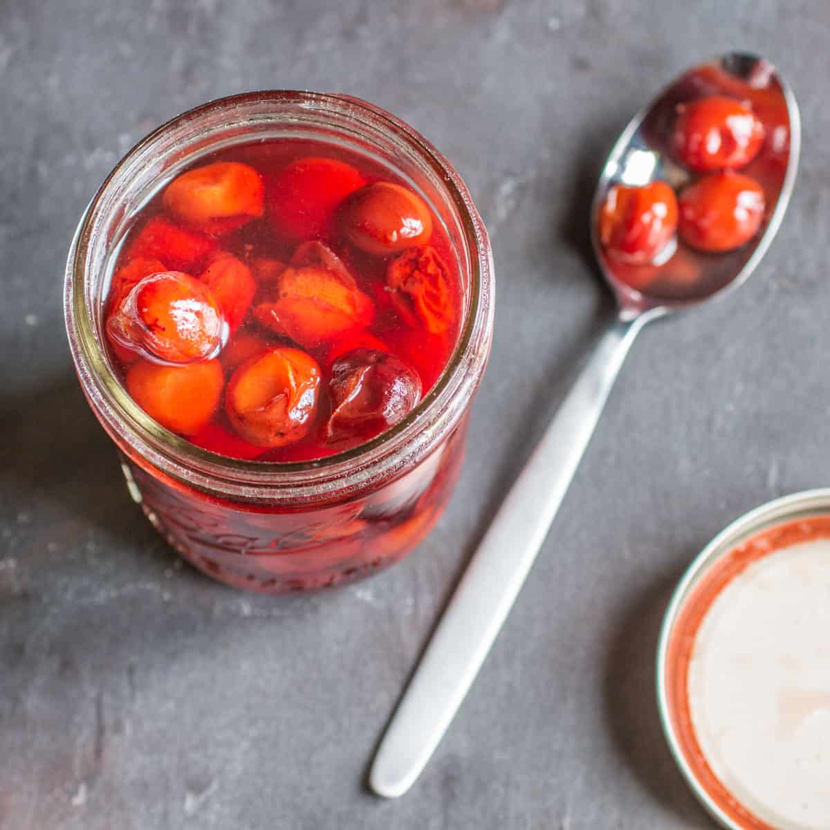 a jar of candied plums with plums on a spoon. 
