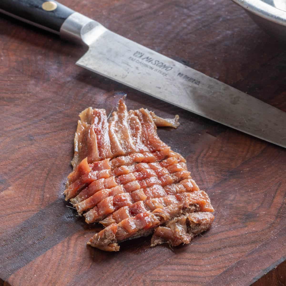 anchovies sliced on a board next to a knife