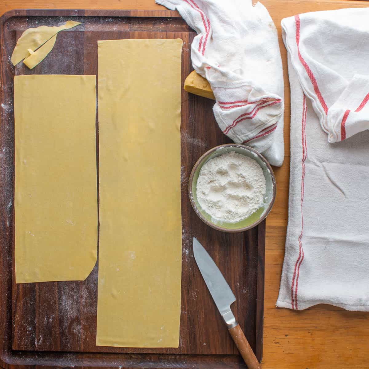 rolled out sheets of pasta with a knife and a bowl of flour