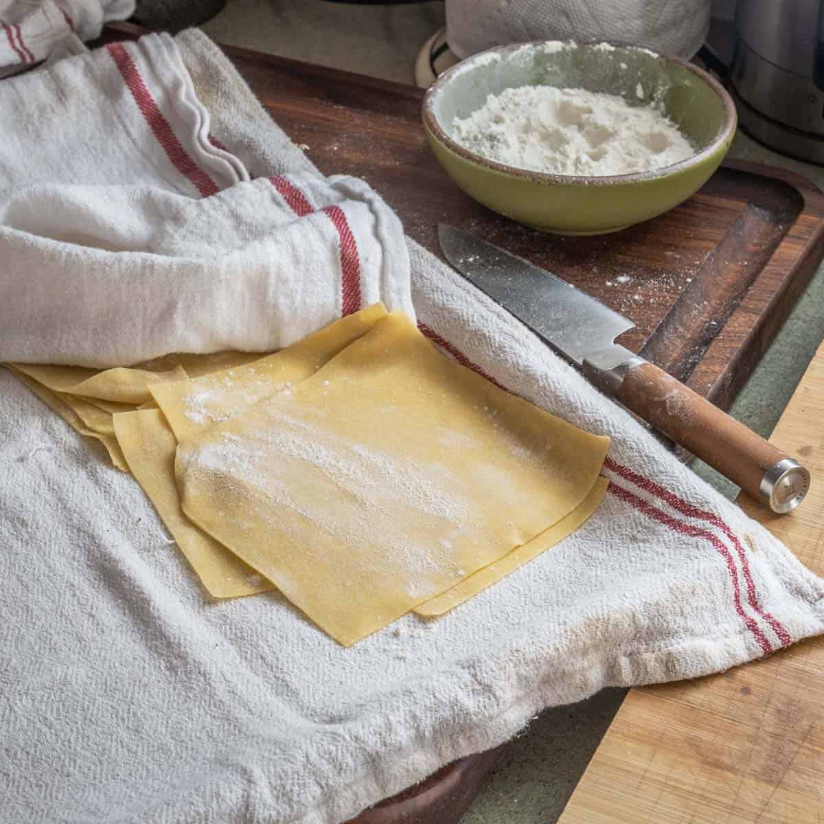 pasta on a tray between towels with a bowl of flour and a knife