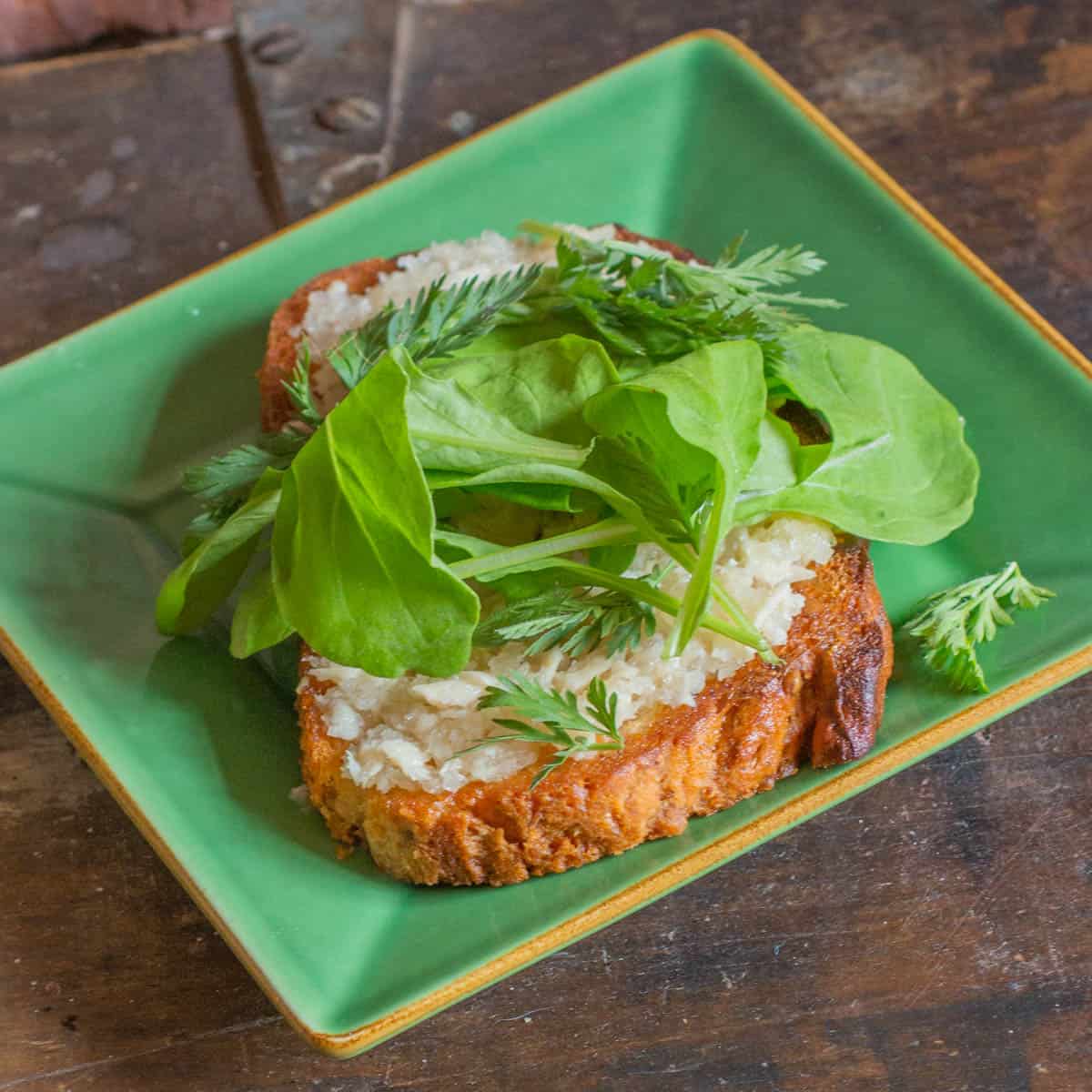 a piece of toast with spread, herbs and greens