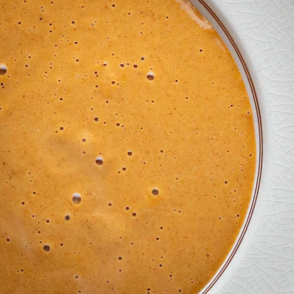 A close up of orange soup in a bowl showing bubbles