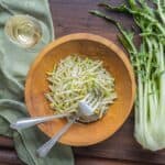 A bowl of sliced white vegetables next to a stalk of chicory and a glass of wine.