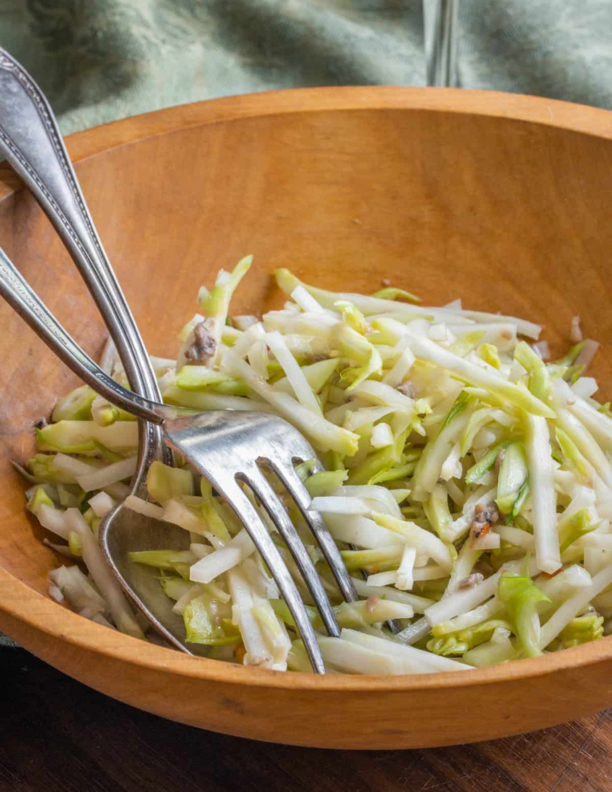 a wooden bowl of sliced vegetables with a green napkin, spoon and fork.