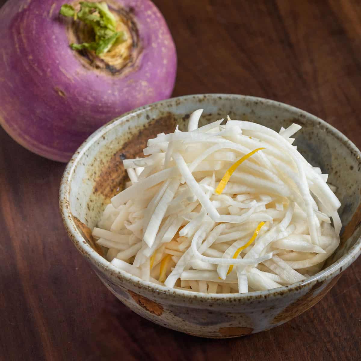 a bowl of shredded fermented turnips next to purple top turnips