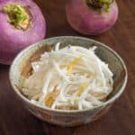 a bowl of shredded fermented turnips next to purple top turnips