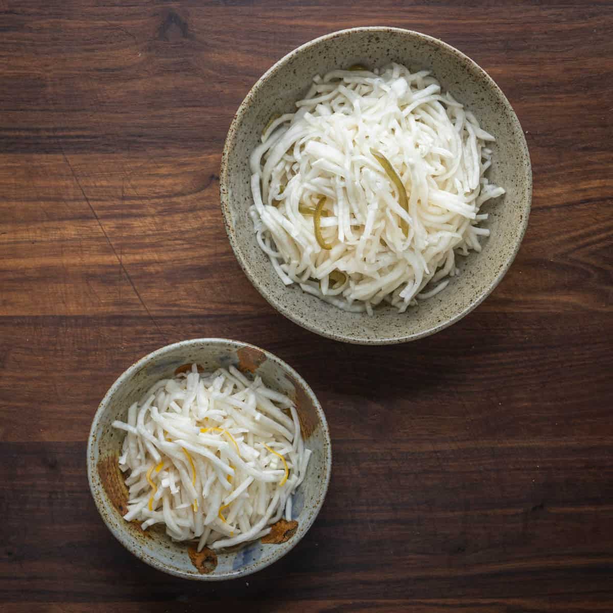 two bowls of thinly sliced fermented turnips.