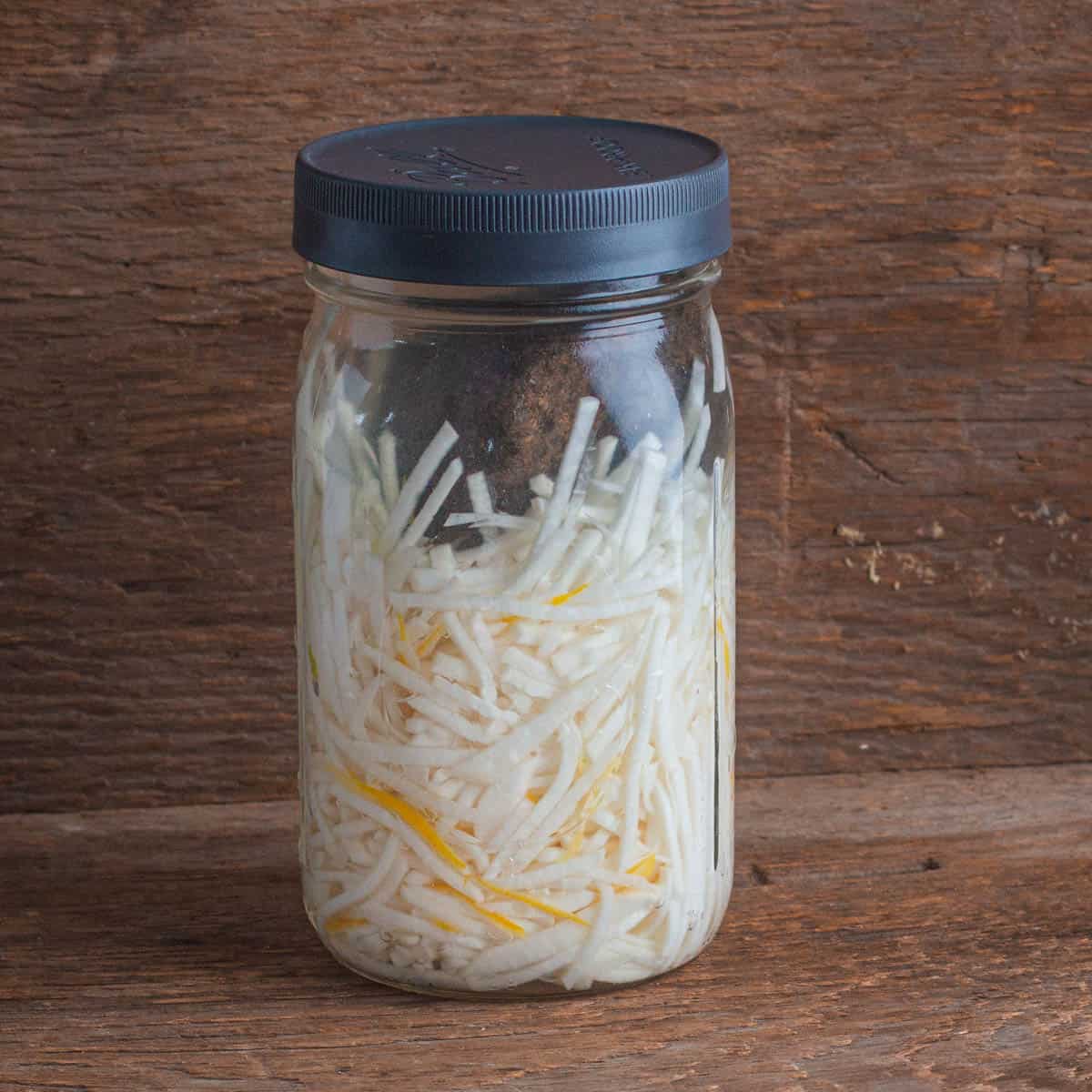 turnips fermenting in brine in a mason jar with a plastic lid