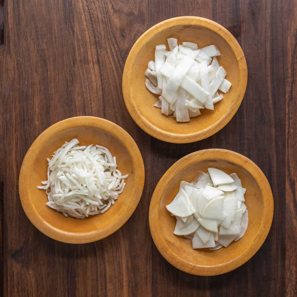 three shapes of cut turnips in wooden bowls.