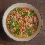 a bowl of wild mushrooms in broth with herbs and pasta