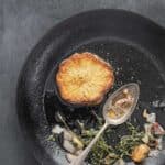 celeriac steak cooking in a pan with herbs and garlic