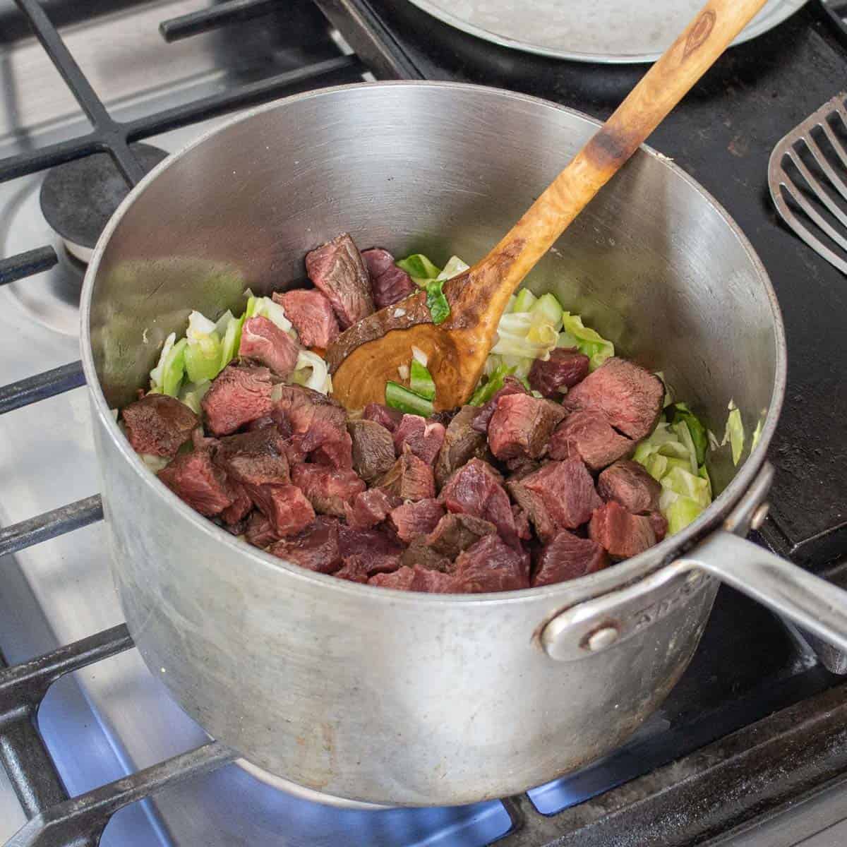 Adding venison to a pot with cabbage and vegetables 