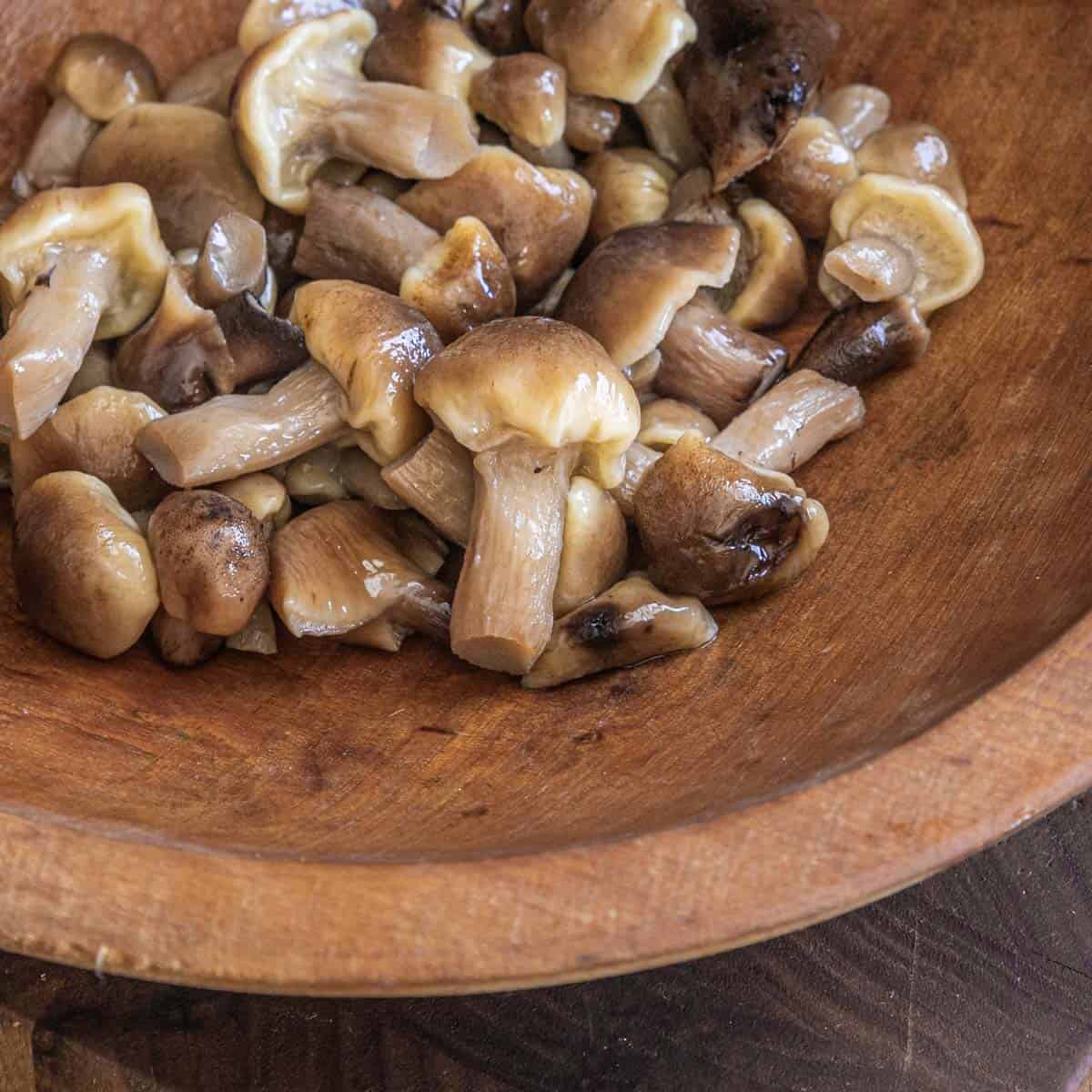close up of cooked honey mushrooms in a wooden bowl.