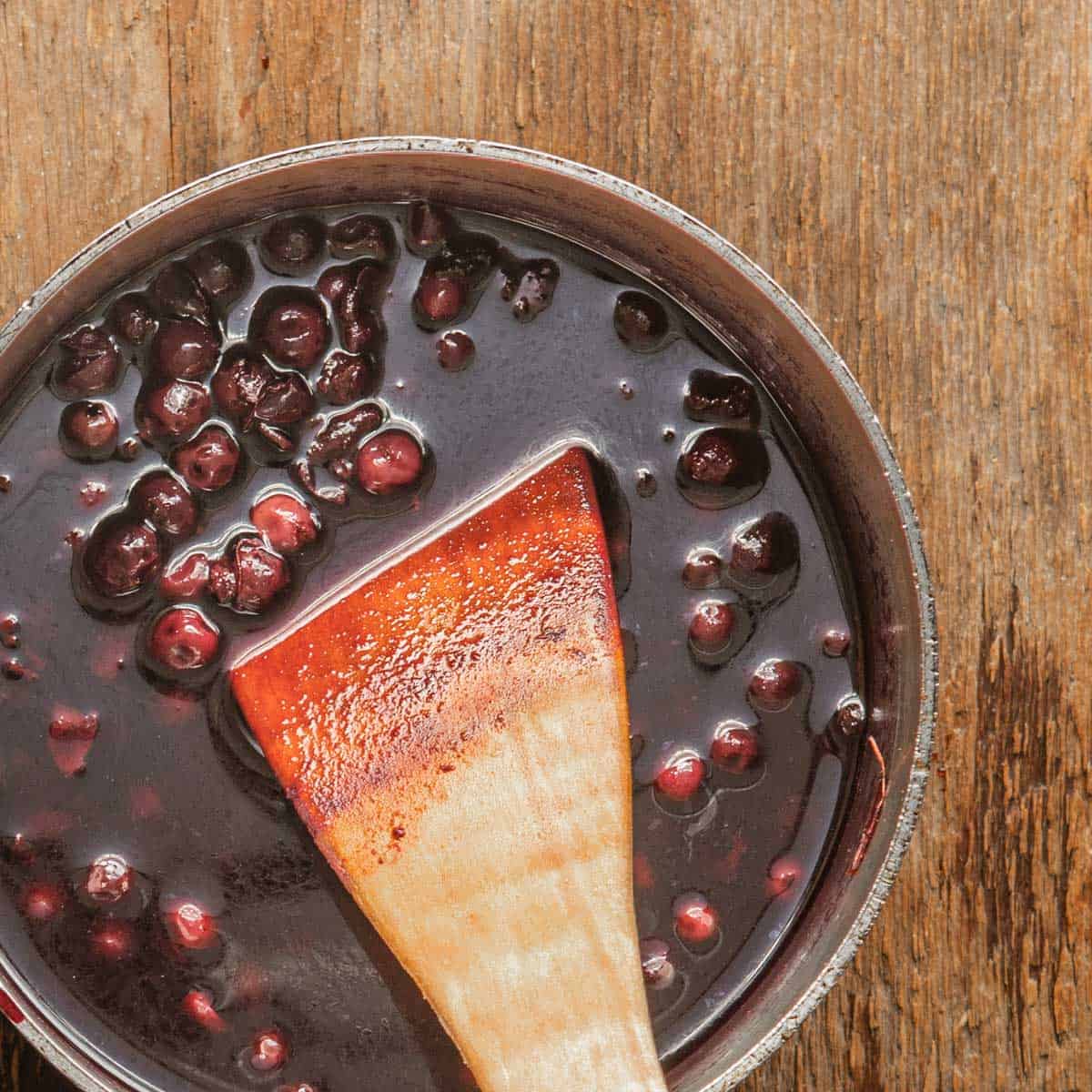 Wild cherries cooking in a pot with a wooden spoon