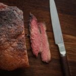 Beef bacon sliced with a knife on a wooden cutting board.