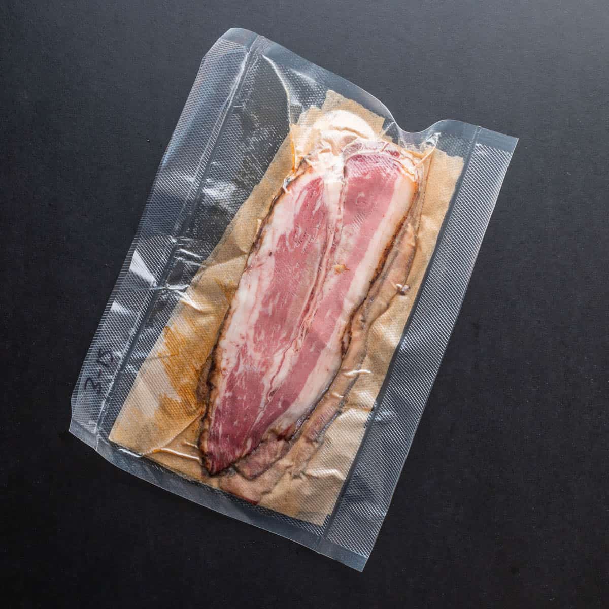 Sliced beef bacon layered in parchment in a vacuum sealed bag.