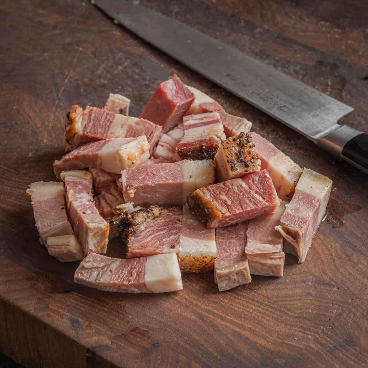 Thick sliced lardons or batons of beef bacon next to a knife on a cutting board.